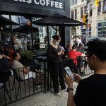 
              People use electronics outside a coffee shop in Toronto amid a nationwide Rogers outage, affecting many of the telecommunication company's services, Friday, July 8, 2022. (Cole Burston/The Canadian Press via AP)
            