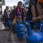 
              A boy tries to lift an empty cylinder as he along with others wait in a queue to buy domestic gas at a distribution center, in Colombo, Sri Lanka, Tuesday, July 12, 2022. A political vacuum continues in Sri Lanka with opposition leaders yet to agree on who should replace its roundly rejected leaders, whose residences are occupied by protesters angry over the country’s deep economic woes. (AP Photo/Rafiq Maqbool)
            