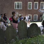 A guide dressed in a Colonial Era costume conducts a tour in the Granary Burying Ground on the Freedom Trail, Friday, June 17, 2022, in Boston. The summer of 2022 can feel as if the coronavirus pandemic is really over. Mask rules and testing requirements are lifting in many countries, including the United States. (AP Photo/Michael Dwyer)