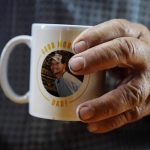 
              Larry Guess holds a mug with his son David Guess' face on Thursday, June 23, 2022, in Athens, Ala. Guess says he uses the mug for coffee everyday and still can't believe his son is gone. David Guess was killed by gun violence in March. (AP Photo/Brynn Anderson)
            
