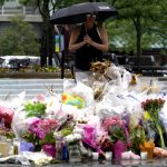 
              A visitor takes comfort during a rainy day at a memorial to the seven people killed and others injured in Port Clinton Square in the Fourth of July mass shooting, in Highland Park, Ill., Friday, July 15, 2022. (AP Photo/Nam Y. Huh)
            