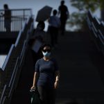 
              A woman wearing a face mask walks across a pedestrian bridge on an unseasonably warm day in Beijing, Thursday, July 14, 2022. High temperatures have prompted cites in eastern China to open former air raid shelters as a relief from the heat. Temperatures have surpassed all-time records in much of the country, while flooding has hit many parts. (AP Photo/Mark Schiefelbein)
            