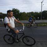 
              People cycle and walk due to roadblocks set up by protesters demonstrating against inflation, especially surging fuel prices, in Pacora, Panama, early Wednesday, July 20, 2022. (AP Photo/Arnulfo Franco)
            