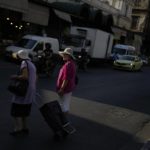 
              Two women wait to cross the road at Varvakios fish market in central Athens, Greece, Friday, Aug. 19, 2022. Saturday's formal end of Greece's close budgetary supervision by European Union creditors closes an unwelcome chapter dating back to the painful bailout years. (AP Photo/Thanassis Stavrakis)
            