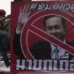 
              An anti-government protester climb on car beside a poster of Prime Minister Prayuth Chan-ocha in Bangkok, Thailand, Wednesday, Aug. 24, 2022. Thailand's Constitutional Court ruled Wednesday that Prime Minister Prayuth Chan-ocha must suspend his active duties while the court decides whether he has overstayed his legal term in office. The poster reads "Time is over." (AP Photo/Sakchai Lalit)
            