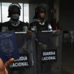 
              FILE - A migrant holds up his Venezuelan passport outside the Border Transit Comprehensive Care Center, guarded by National Guards, to ask for legal documents that allow his group to travel through Mexico, on the outskirts of Huixtla, Chiapas state, Mexico, June 10, 2022, after the group left Tapachula by foot five days prior, tired of waiting to normalize their status in a region with little work, with the ultimate goal of reaching the US. Mexico has employed a strategy of containment, since the Trump administration, meant to keep migrants confined to the south, far from the U.S. border.  (AP Photo/Marco Ugarte, File)
            