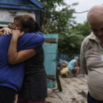 
              Nina Bilyk, left, is embraced by her friend, Olga Gurina, as she mourns the loss of her partner, Ivan Fartukh, along with his cousin, Andrii Fartukh, right, at their home Saturday, Aug. 13, 2022, where he was killed in a Russian rocket attack last night in Kramatorsk, Donetsk region, eastern Ukraine. The strike killed three people and wounded 13 others, according to the mayor. The attack came less than a day after 11 other rockets were fired at the city. (AP Photo/David Goldman)
            