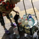 
              Lyubov Mahlii, 76, packs a crate with water bottles she filled up at a public tank to take back to her apartment in Sloviansk, Donetsk region, eastern Ukraine, Saturday, Aug. 6, 2022. "When there are bombings and sirens, we keep carrying it," she said. "It's a great risk for us, but what can we do?" (AP Photo/David Goldman)
            