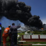 
              Workers of the Cuba Oil Union, known by the Spanish acronym CUPET, watch a huge rising plume of smoke from the Matanzas Supertanker Base, as firefighters work to quell a blaze which began during a thunderstorm the night before, in Matazanas, Cuba, Saturday, Aug. 6, 2022. Cuban authorities say lightning struck a crude oil storage tank at the base, causing a fire that led to four explosions which injured more than 50 people. (AP Photo/Ramon Espinosa)
            