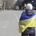 
              FILE - A woman covered by Ukrainian flag stands in front of Russian troops in a street during a rally against Russian occupation in Kherson, Ukraine, Saturday, March 19, 2022. The southern city of Kherson was the first to fall to Russia's invasion. But Kherson remains at the heart of the conflict and Ukraine's efforts to save its vital access to the sea. (AP Photo/File)
            