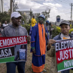 
              Supporters of presidential candidate Raila Odinga gather outside the Supreme Court, one holding a sign in Swahili reading "Democracy Now", left, in Nairobi, Kenya Monday, Aug. 22, 2022. Odinga filed a Supreme Court challenge to last week's election result, asserting that the process was marked by criminal subversion and seeking that the outcome be nullified and a new vote be ordered. (AP Photo/Ben Curtis)
            