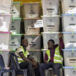
              Electoral workers sit next to stacked ballot boxes after they were received at a tallying center in Nairobi, Kenya, Thursday, Aug. 11, 2022. Kenyans are waiting for the results of a close presidential election in which the turnout was lower than usual. (AP Photo/Ben Curtis)
            