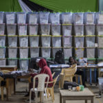 
              Electoral workers sit next to stacked ballot boxes after tallying finished in the Shauri Moyo area of Nairobi, Kenya Friday, Aug. 12, 2022. Kenyans are waiting for the results of a close presidential election in which the turnout was lower than usual. (AP Photo/Ben Curtis)
            