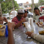 
              Frank Fernandez eats, center, as he laughs with friends at the Colombian-Venezuelan Foundation "Nueva Ilusión", near the border with Venezuela, in Los Patios, Colombia, Saturday, Aug. 6, 2022. Colombian-Venezuelan Foundation "Nueva Ilusión" is a place where food is given to needy people in the community and migrants, mostly Venezuelans, who walk to nearby cities. (AP Photo/Matias Delacroix)
            