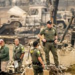 Sheriff's Deputy Johnson stands at a burned home as search and rescue workers recover the remains of a McKinney Fire victim on Monday, Aug. 1, 2022, in Klamath National Forest, Calif. (AP Photo/Noah Berger)