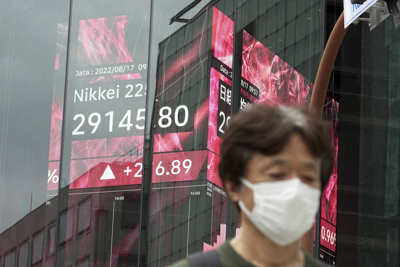 A person wearing a protective mask walks past an electronic stock board showing Japan's Nikkei 225 ...