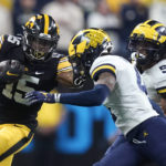 
              FILE - Iowa running back Tyler Goodson (15) runs from Michigan defensive back Vincent Gray, center, and defensive back DJ Turner (5) during the second half of the Big Ten championship NCAA college football game, Saturday, Dec. 4, 2021, in Indianapolis. The Big Ten announced Thursday, Aug. 18, 2022, that it has reached seven-year agreements with Fox, CBS and NBC to share the rights to the conference's football and basketball games. (AP Photo/Darron Cummings, File)
            