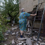 
              Lybov Miroshnik, 74, holds the ladder for a worker repairing the roof of her damaged home Thursday, Aug. 18, 2022, from a rocket strike yesterday in Druzhkivka, Donetsk region, eastern Ukraine, as Russian shelling continued to hit towns and villages in Donetsk province, regional officials said. (AP Photo/David Goldman)
            