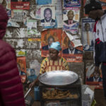 
              A food vendor serves customers as she sits in front of electoral posters in Kibera neighborhood, a stronghold for presidential candidate Raila Odinga, in Nairobi, Kenya, Thursday, Aug. 11, 2022. Kenyans are waiting for the results of a close presidential election in which the turnout was lower than usual. (AP Photo/Mosa'ab Elshamy)
            
