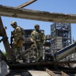 
              FILE - Russian soldiers walk through the debris of the Metallurgical Combine Azovstal, in Mariupol, on the territory which is under the Government of the Donetsk People's Republic control, eastern Ukraine, Monday, June 13, 2022. Despite getting bogged down in Ukraine, the Kremlin has resisted announcing a full-blown mobilization, a move that could prove to be very unpopular for President Vladimir Putin. That has led instead to a covert recruitment effort that includes trying to get prisoners to make up for the manpower shortage. This photo was taken during a trip organized by the Russian Ministry of Defense. (AP Photo, File)
            