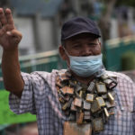
              Anti-government protester wearing amulets around his neck displays the three-finger symbol of resistance during a protest in Bangkok, Thailand, Wednesday, Aug. 24, 2022. Thailand's Constitutional Court ruled Wednesday that Prime Minister Prayuth Chan-ocha must suspend his active duties while the court decides whether he has overstayed his legal term in office. (AP Photo/Sakchai Lalit)
            