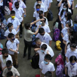 
              A teacher conducts temperature checks on students during the opening of classes at the San Juan Elementary School in Pasig, Philippines on Monday, Aug. 22, 2022. Millions of students wearing face masks streamed back to grade and high schools across the Philippines Monday in their first in-person classes after two years of coronavirus lockdowns that are feared to have worsened one of the world's most alarming illiteracy rates among children. (AP Photo/Aaron Favila)
            