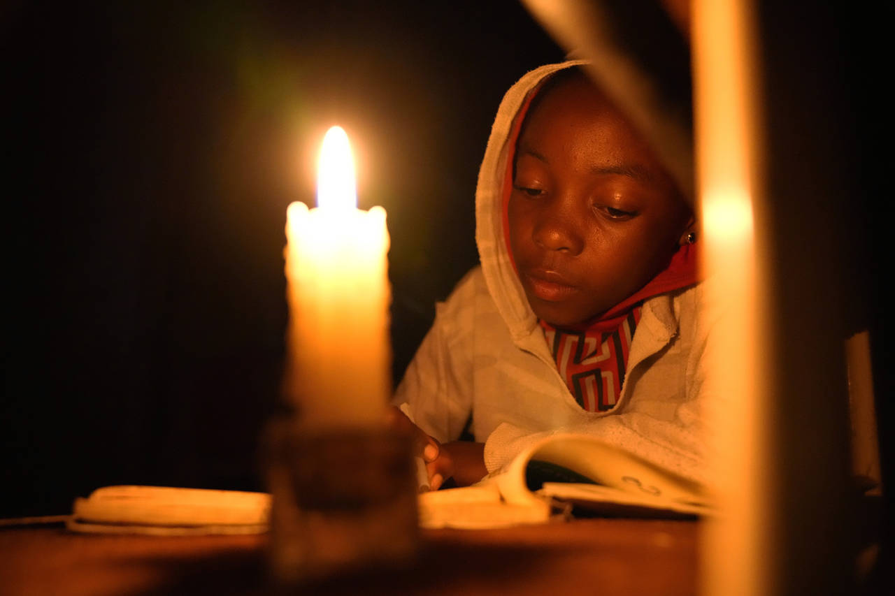 Tracy Carlos uses a candlelight to do her homework in Mabvuku on the outskirts of Harare on Wednesd...