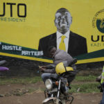 
              Kenyan Boda Boda motor cycle riders wait near a large mural of William Ruto, a contesting bid for president, in Eldoret, Kenya, Friday, Aug.12, 2022. Kenyans are waiting for the results of a close presidential election in which the turnout was lower than usual. (AP Photo/Brian Inganga)
            
