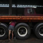 
              Worker Doris Parra cleans a flatbed truck on the property of veteran businessman Alfredo Rosales in San Juan de Colon, Venezuela, Thursday, Aug. 4, 2022, on the Colombian border. Rosales said he had a prosperous fleet of over 50 trucks before the border was partially closed by the Venezuelan government in 2015, but had to downsize to four trucks and sell the rest as scrap as the Colombian-coal import business dropped. (AP Photo/Matias Delacroix)
            