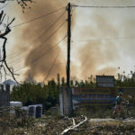 
              A local resident pushes his bike as smoke rises over the site of an explosion after a rocket attack in Bakhmut, Donetsk region, Ukraine, Wednesday, Aug. 31, 2022. (AP Photo/Kostiantyn Liberov)
            