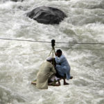 
              People cross a river on a suspended cradle, in the town of Bahrain, Pakistan, Tuesday, Aug. 30, 2022. The United Nations and Pakistan issued an appeal Tuesday for $160 million in emergency funding to help millions affected by record-breaking floods that have killed more than 1,150 people since mid-June. (AP Photo/Naveed Ali)
            