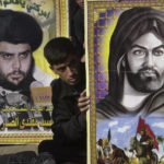 
              FILE - An Iraqi sits between posters of prominent Shiite cleric Sheik Muqtada al-Sadr, left, and Imam Ali, the first Imam and cousin of prophet Muhammed during Friday prayers in the largest Shiite Muslim enclave in Baghdad, Friday Nov. 14, 2003. Al-Sadr is a populist cleric, who emerged as a symbol of resistance against the U.S. occupation of Iraq after the 2003 invasion. ( AP Photo/Samir Mizban, File)
            