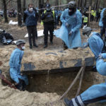 
              Emergency workers move a body during the exhumation in the recently retaken area of Izium, Ukraine, Friday, Sept. 16, 2022. Ukrainian authorities discovered a mass burial site near the recaptured city of Izium that contained hundreds of graves. It was not clear who was buried in many of the plots or how all of them died, though witnesses and a Ukrainian investigator said some were shot and others were killed by artillery fire, mines or airstrikes. (AP Photo/Evgeniy Maloletka)
            