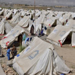 
              Victims of heavy flooding from monsoon rains stand beside their tents at a relief camp in Dasht near Quetta, Pakistan, Friday, Sept. 16, 2022. The devastating floods affected over 33 million people and displaced over half a million people who are still living in tents and make-shift homes. The water has destroyed 70% of wheat, cotton and other crops in Pakistan. (AP Photo/Arshad Butt)
            