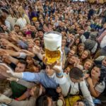 
              Young people reach out for free beer in one of the beer tents on the opening day of the 187th Oktoberfest beer festival in Munich, Germany, Saturday, Sept. 17, 2022. Oktoberfest is back in Germany after two years of pandemic cancellations, the same bicep-challenging beer mugs, fat-dripping pork knuckles, pretzels the size of dinner plates, men in leather shorts and women in cleavage-baring traditional dresses.  (AP Photo/Michael Probst)
            