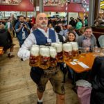 
              A waiter carries beer in one of the beer tents on the opening day of the 187th Oktoberfest beer festival in Munich, Germany, Saturday, Sept. 17, 2022. Oktoberfest is back in Germany after two years of pandemic cancellations, the same bicep-challenging beer mugs, fat-dripping pork knuckles, pretzels the size of dinner plates, men in leather shorts and women in cleavage-baring traditional dresses. (AP Photo/Michael Probst)
            
