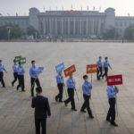 
              Staff members carrying signs walk across Tiananmen Square before a ceremony to mark Martyr's Day in Beijing, Friday, Sept. 30, 2022. (AP Photo/Mark Schiefelbein)
            