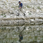 
              Fisherman Nick Gann walks along the receding edge of Flaming Gorge Reservoir in Wyoming on Friday, Aug. 5, 2022. A boating and fishing paradise on the Utah-Wyoming line, Flaming Gorge is beginning to feel the effects of the two-decade megadrought gripping the southwestern U.S. (AP Photo/Rick Bowmer)
            