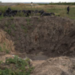 An employee walks nearby a crater created by an explosion on a field at the Veres farm in Novomykolaivka, eastern Ukraine, Saturday, Sept. 10, 2022. All work has halted on this large eastern Ukrainian farm, whose fields and compound have been hit so many times by mortars, rockets, missiles and cluster bombs that its workers are unable to sow the crater-scarred land or harvest any crops. (AP Photo/Leo Correa)