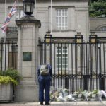 
              A man bows as another leave flowers outside the British Embassy following the death of Queen Elizabeth II, Friday, Sept. 9, 2022, in Tokyo. Queen Elizabeth II, Britain's longest-reigning monarch and a rock of stability across much of a turbulent century, died Thursday after 70 years on the throne. She was 96. (AP Photo/Eugene Hoshiko)
            