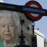 
              FILE - In this April 9, 2020 file photo an image of Britain's Queen Elizabeth II and quotes from her historic television broadcast commenting on the coronavirus pandemic are displayed on a big screen behind the Eros statue and a London underground train station entrance sign at Piccadilly Circus in London. Queen Elizabeth II, Britain’s longest-reigning monarch and a rock of stability across much of a turbulent century, has died. She was 96. Buckingham Palace made the announcement in a statement on Thursday Sept. 8, 2022. (AP Photo/Kirsty Wigglesworth, File)
            