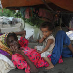 
              A woman and child rest next to their home damaged by monsoon rains in Hyderabad, Pakistan, Monday, Sept. 12, 2022. Pakistan is grappling with food shortages after deadly floods left the impoverished country's agriculture belt underwater, the prime minister told the Turkish president by phone, as authorities scaled up efforts Monday to deliver food, tents and other items. (AP Photo/Pervez Masih)
            