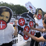 Protesters, two of them wearing masks of U.S. Vice President Kamala Harris and South Korean President Yoon Suk Yeol, stage a rally to oppose a visit by Harris as their colleague puts a sticker on a banner in front of the presidential office in Seoul, South Korea, Thursday, Sept. 29, 2022. (AP Photo/Ahn Young-joon)