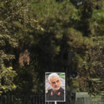 An Iranian pro-government demonstrator holds a poster of the late Revolutionary Guard Gen. Qassem Soleimani, who was killed in Iraq in a U.S. drone attack in 2020, in a rally after the Friday prayers to condemn recent anti-government protests over the death of a young woman in police custody as they hold Iranian flags and in Tehran, Iran, Friday, Sept. 23, 2022. The crisis unfolding in Iran began as a public outpouring over the the death of Mahsa Amini, a young woman from a northwestern Kurdish town who was arrested by the country's morality police in Tehran last week for allegedly violating its strictly-enforced dress code. (AP Photo/Vahid Salemi)