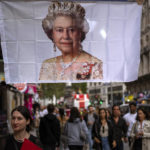 
              People walk past a flag with a portrait of Queen Elizabeth II in central London, Monday, Sept. 12, 2022. Queen Elizabeth II, Britain's longest-reigning monarch and a rock of stability across much of a turbulent century, died Thursday Sept. 8, 2022, after 70 years on the throne. She was 96. (AP Photo/Emilio Morenatti)
            