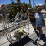 
              Debbie and Lou Evans push their dog Brody on a hotel luggage cart they found amidst the wreckage, as they come to check on their home, two days after the passage of Hurricane Ian, in Fort Myers Beach, Fla., Friday, Sept. 30, 2022. (AP Photo/Rebecca Blackwell)
            