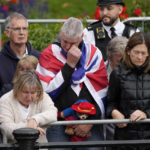
              A person holding a Paddington Bear stuffed toy stands with members of the public outside Buckingham Palace waiting to watch Queen Elizabeth II funeral procession, in central London Monday, Sept. 19, 2022. The Queen, who died aged 96 on Sept. 8, will be buried at Windsor alongside her late husband, Prince Philip, who died last year. (AP Photo/Christophe Ena, Pool)
            