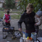 
              Margaryta Tkachenko, 29 years old, prepares food on the open fire for her 9-month-old daughter Sophia in the recently retaken town of Izium, Ukraine, Sunday, Sept. 25, 2022. (AP Photo/Evgeniy Maloletka)
            