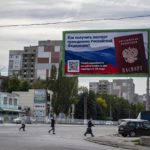 
              People cross a street with a billboard reading "How to get a passport of a citizen of Russia" prior to a referendum in Luhansk, Luhansk People's Republic controlled by Russia-backed separatists, eastern Ukraine, Thursday, Sept. 22, 2022. Authorities in Russian-controlled regions in eastern and southern Ukraine are preparing to hold referendums on becoming part of Russia's a move that could allow Moscow to escalate the war. The votes start Friday in the Luhansk, Kherson and partly Russian-controlled Zaporizhzhia and Donetsk regions. (AP Photo)
            