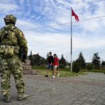 
              FILE - A young couple walks past a Russian soldier guarding an area at the Alley of Glory exploits of the heroes - natives of the Kherson region, who took part in the liberation of the region from the Nazi invaders, in Kherson, Kherson region, south Ukraine, Friday, May 20, 2022, with a replica of the Victory banner marking the 77th anniversary of the end of World War II right in the background. Ukrainian forces pressing an offensive in the south have zeroed in on Kherson, a provincial capital that has been under Russian control since the early days of the invasion. This photo was taken during a trip organized by the Russian Ministry of Defense. (AP Photo, File)
            